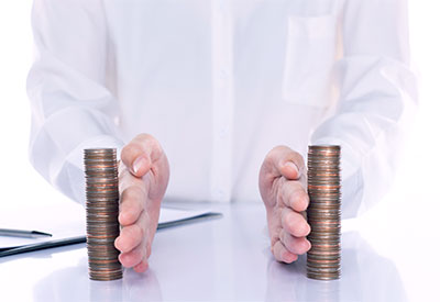 A person in a white shirt with only hands visible is organizing two tall stacks of coins on a reflective surface, meticulously arranging the assets. The hands are placed on either side, guiding the coins into neatly aligned piles. A pen lies on the table in the background.