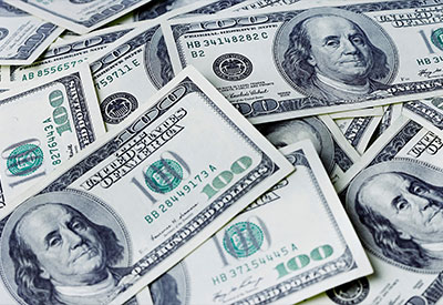 A scattered pile of U.S. one hundred dollar bills, commonly seen in discussions around estate planning and inheritance, features a portrait of Benjamin Franklin. The predominant colors are green and white, with the image focusing on the money, showing various angles and parts of notes overlapping each other.