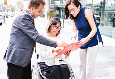 Two professionals assist a woman in a wheelchair with estate planning, focusing on long-term care and financial stability for her future
