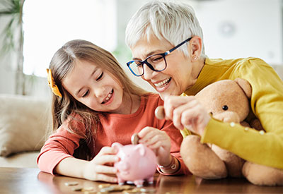 A smiling elderly woman with glasses and a young girl are sitting at a table, engaged in playful estate planning.