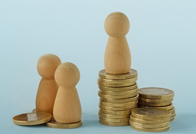 A wooden figure stands atop a stack of gold coins while two others stand on the ground, symbolizing estate distribution, inheritance planning, and financial inequality among heirs.