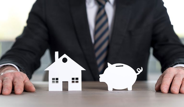 a man standing behind a graphic of a house and a piggy bank