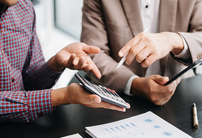 Two individuals discuss financial documents and use a calculator, highlighting life insurance, estate planning, and preparation for estate taxes and liquidity needs.