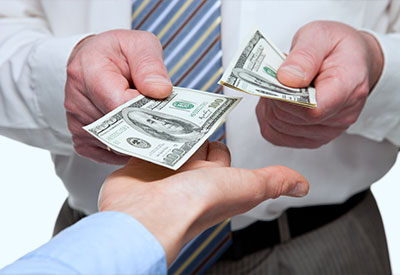 Close-up of two individuals exchanging cash. One person wearing a white shirt and striped tie hands over two $100 bills, addressing a debt, while the other person in a light blue shirt receives the money, only their hand visible in the frame.