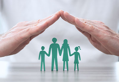 A pair of hands hovers protectively over a green paper cutout illustration of a family of four, consisting of two adults and two children. The image symbolizes protection, security, and the importance of estate planning for your loved ones' future.
