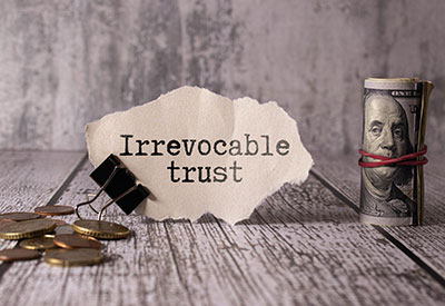A concept of financial planning with a note labeled 'Irrevocable trust' next to a roll of money and coins, highlighting asset protection and tax minimization strategies in estate planning.
