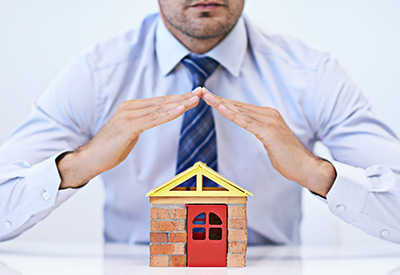 A man protecting a model house with his hands, symbolizing estate planning and the security of trusts post-divorce.