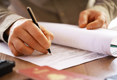 A person's hand writing on a document, suggesting paperwork or form completion related to estate planning or legal matters.