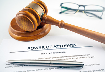 A wooden gavel next to a 'Power of Attorney' document and eyeglasses, representing legal authority and decision-making in estate planning.