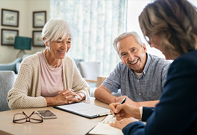 An elderly couple sits at a table, smiling warmly as they discuss estate planning with a professional woman