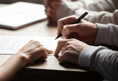 Two people discussing a document on a table, with one person pointing at a section while the other holds a pen, ready to write. focus on their hands and the paper.