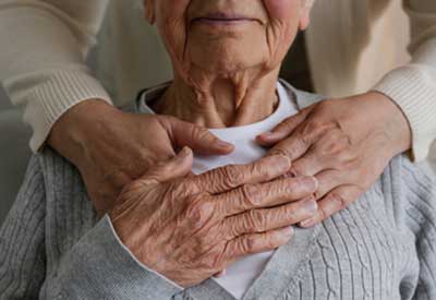 An elderly person's hands are clasped over their chest in a gesture that suggests gratitude, comfort, or memory