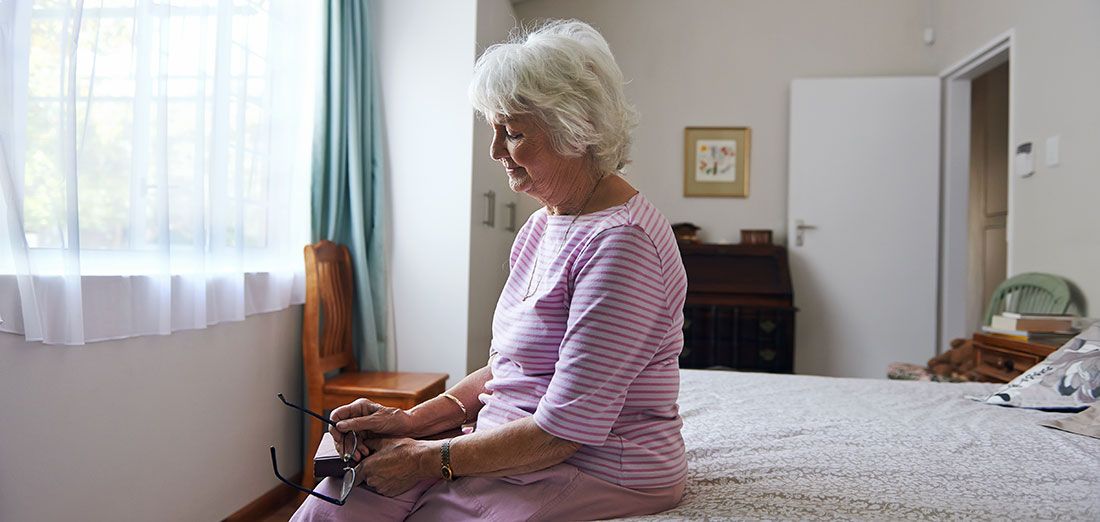 Health - Senior woman sitting on a bed alone