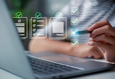 A person types on a laptop while digital checklist icons and document graphics float above the screen