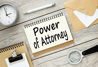 A desktop workspace featuring a notepad with 'Power of Attorney' written on it, alongside office supplies, a clock, and paperclips on a wooden surface.