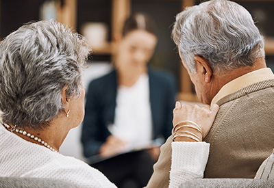 An elderly couple sits across from a professional advisor, likely discussing power of attorney and estate planning matters in a consultation setting.