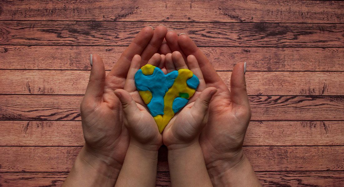 a pair of little hands ontop of a pair of adult hands holding a heart made out of clay