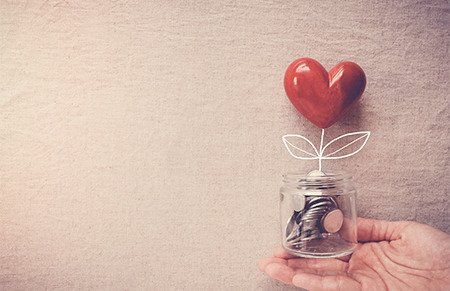 someones hand holding a jar with coins inside and a flower shaped as a heart ontop of the jar