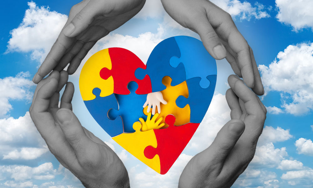 An illustration of two hands forming a protective shape around a heart made up of colorful puzzle pieces, with smaller hands inside the heart. The background features a bright blue sky with clouds, symbolizing care and support for children with special needs.