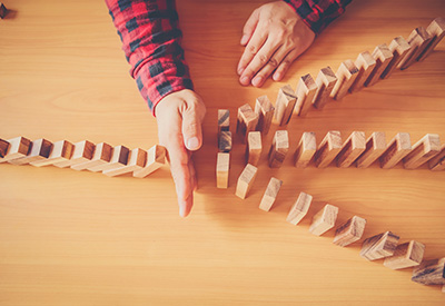 A person in a red and black checkered shirt interrupting a chain of tumbling wooden blocks