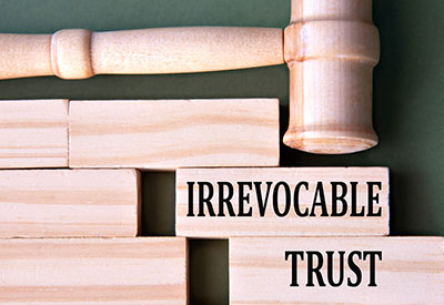 Wooden blocks labeled 'Irrevocable Trust' with a gavel, symbolizing the importance of irrevocable trusts in protecting assets from estate recovery and meeting Medicaid's 'any circumstances' test.