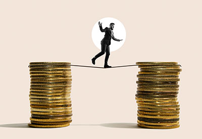 A man balancing precariously on a tightrope stretched between two stacks of coins, representing the risks involved when the grantor acts as the trustee.
