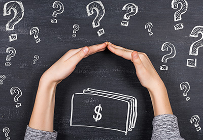 Hands forming a protective roof gesture over a chalk-drawn dollar bill on a blackboard surrounded by question marks