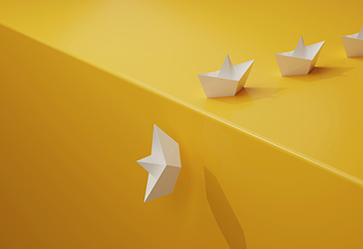 White paper boats on a yellow surface with one boat heading in a different direction