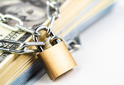 A stack of US dollar bills is wrapped in a silver chain secured with a brass padlock, symbolizing the concept of financial security or restriction, highlighting the importance of income trust.