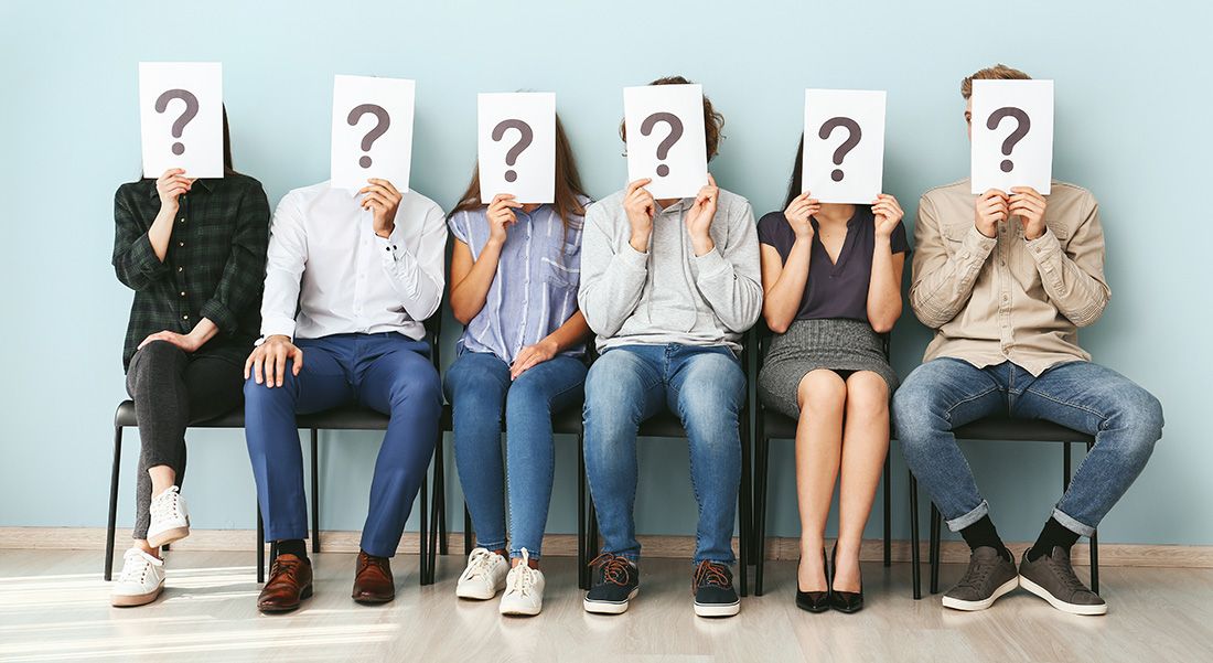a group of people sitting next to each other holding up signs with question marks on them