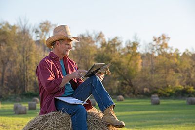 Conservation easement - Farmer sitting on a hay bail looking at a tablet