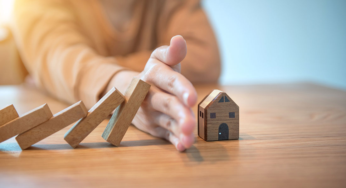 A hand out, preventing dominoes from falling onto a toy house.