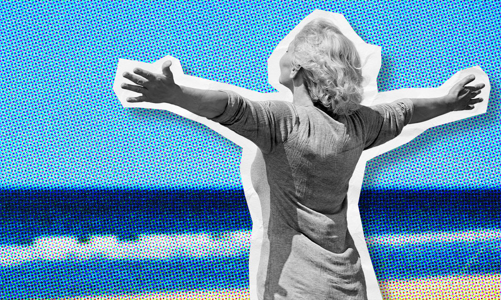 A woman stands with her arms spread out reaching to the sky on a beach