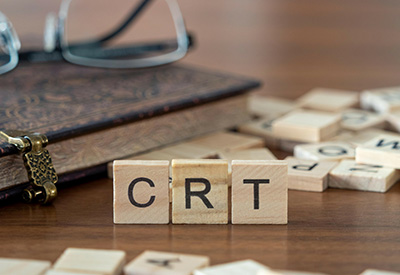 Wooden letter tiles spelling 'CRT' on a desk signify Charitable Remainder Trusts, a tool in charitable estate planning to reduce estate tax and support charitable organizations.