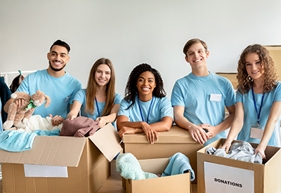 A diverse group of five smiling volunteers wearing blue shirts surrounded by donation boxes, embodying the spirit of charitable giving and community support in legacy planning.