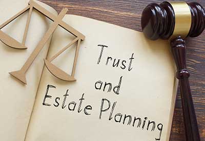 A gavel and a scale of justice next to a notebook labeled 'Trust and Estate Planning'.
