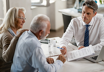A professional in a suit discusses documents with an elderly couple, likely related to estate planning, wills, or financial matters.