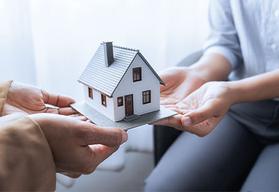 In a softly lit interior, two people hold a scale model of a house together, symbolizing collaboration in estate planning and the journey toward homeownership.