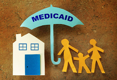 Paper cutouts depict a house, a family, and an umbrella labeled 'Medicaid.'