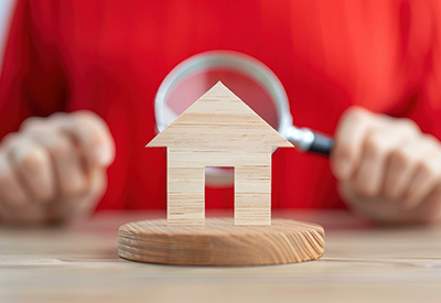 A magnifying glass over a small wooden house, representing careful review of homestead laws and protections for homeowners.