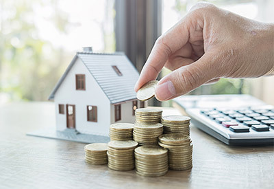 several stacks of coins with a model home and calculator on a desk