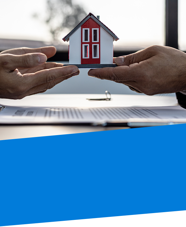two pair of hands holding a model home over paper work