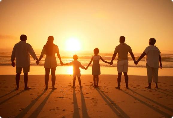 Family holding hands and standing in a line on the beach, watching a beautiful sunset over the ocean.